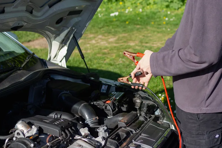 Persona conecta las pinzas de los cables de arranque a la batería de un auto con el capó abierto