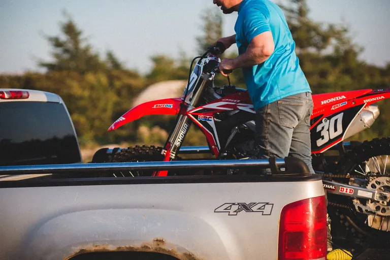 Hombre sube una moto todoterreno a la tolva de una camioneta pickup al atardecer