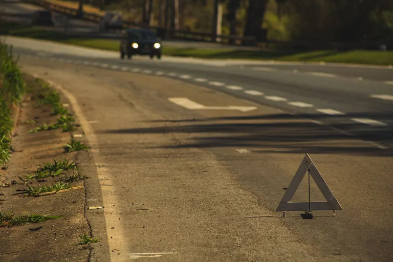 Triángulo de seguridad en el borde de una carretera al atardecer, con un auto que se acerca
