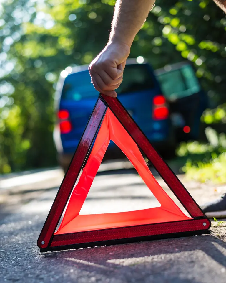 Mano coloca un triángulo de seguridad reflectante en la pista detrás de un auto detenido